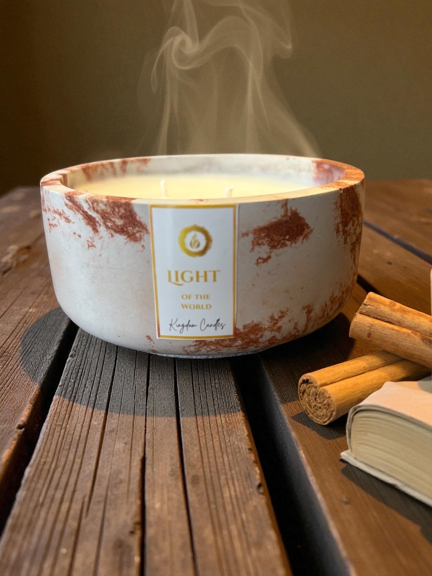 Candle with a label on a wooden surface with cinnamon sticks and a book