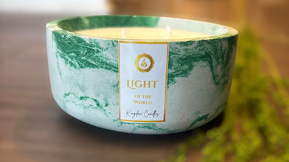Marble-patterned candle with 'Light of the World' branding on a wooden surface.